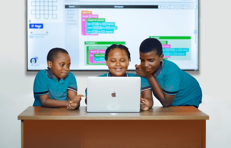 Three KodeUni students working together on a laptop, with their code on the screen behind them